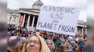 A crowd of people protest in front of a government building. In the middle, someone holds a sign reading 