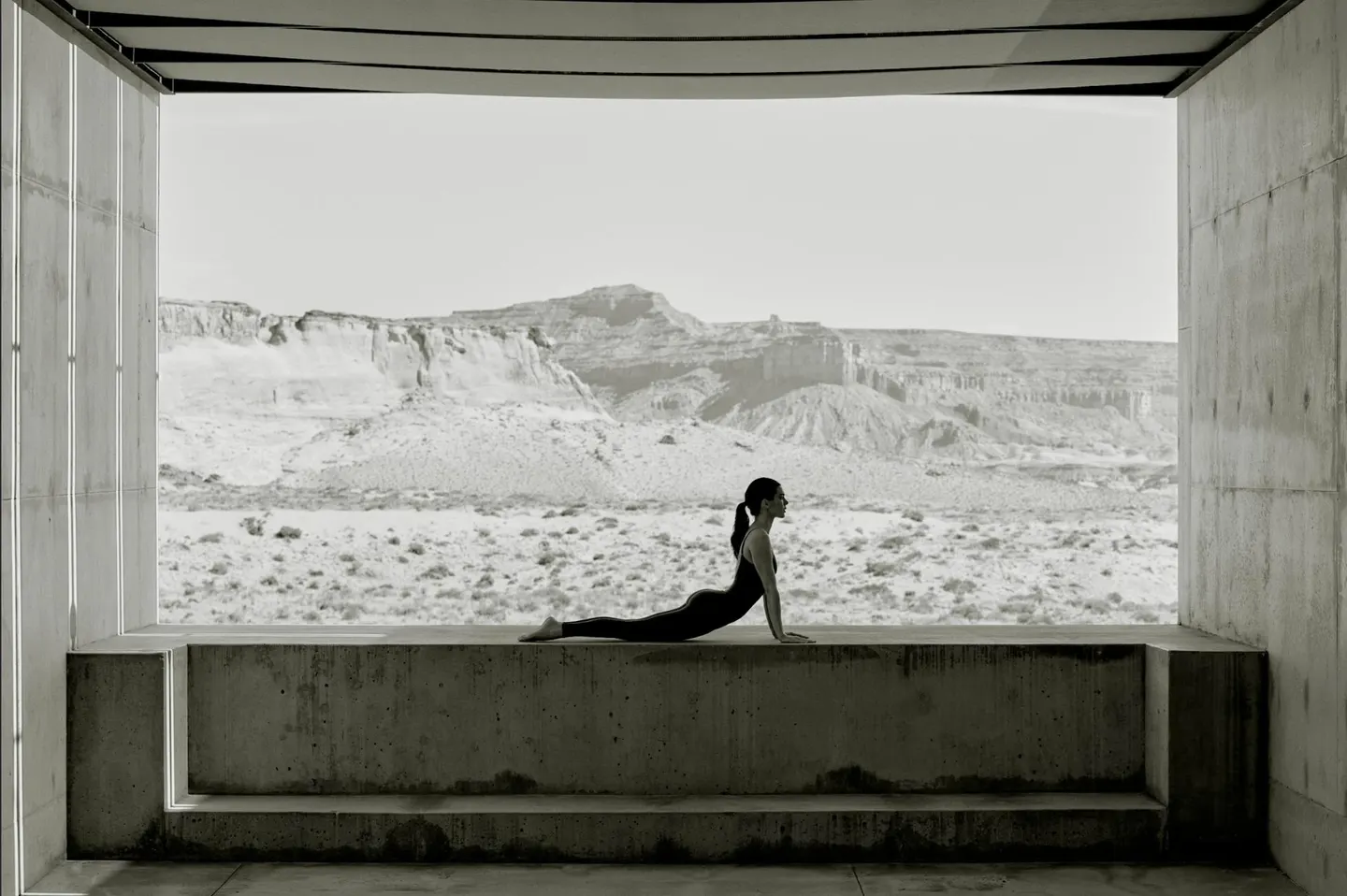 Kendall Jenner does yoga in an open concrete structure overlooking a desert landscape, captured in black and white.